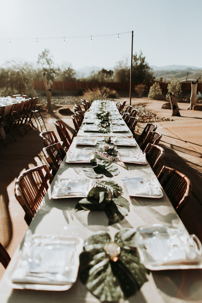 A Joshua Tree wedding reception at Tumbleweed Sanctuary, long farm tables with monstera leaf centerpieces