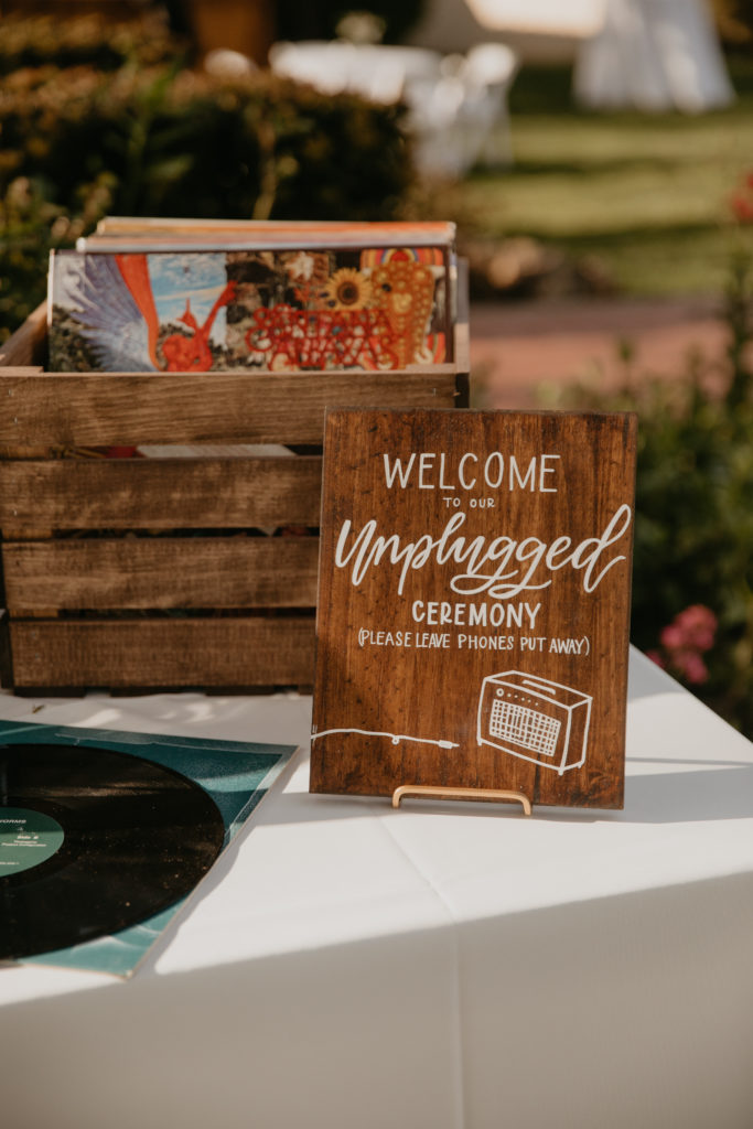 A music festival themed wedding ceremony at The Inn at Rancho Santa Fe, welcome table with record guest book, unplugged ceremony sign