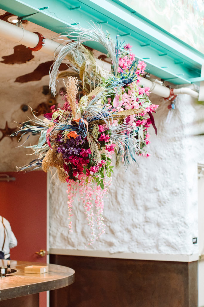 A unique and colorful wedding cocktail hour at the Grass Room in downtown Los Angeles, eclectic floral hanging installation above bar