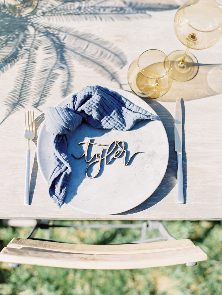 A California-cool rehearsal dinner at Calamigos Ranch, natural farm table with blue napkins and drink ware, custom name cards