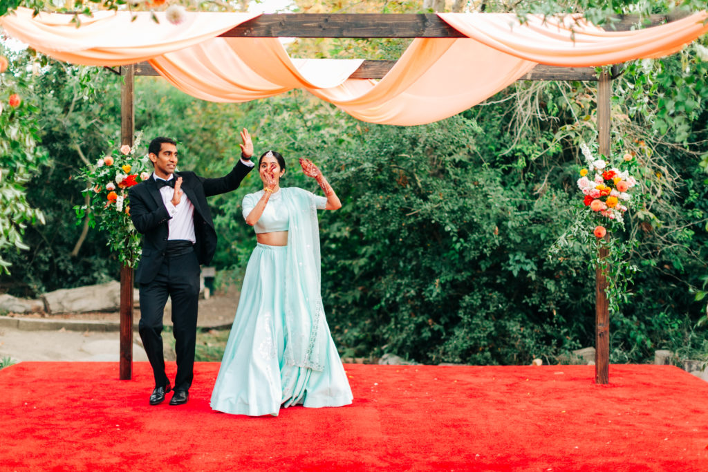 bride in teal wedding saree and groom in black suit portrait shot in front of mandap
