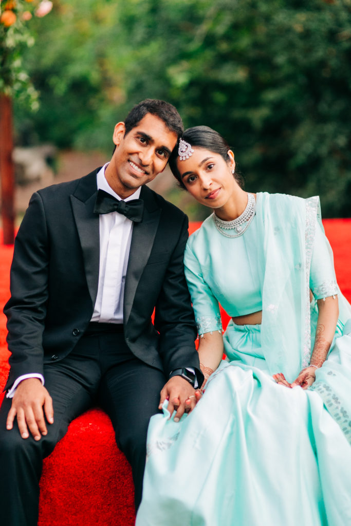 bride in teal wedding saree and groom in black suit portrait shot in front of mandap