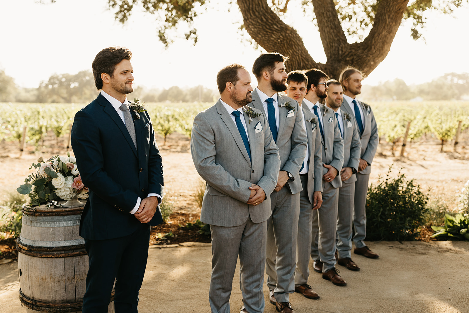 groom stands with groomsmen in grey suits and blue ties