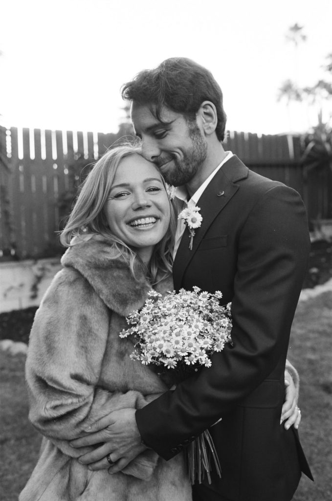 bride in fur coat and daisy bouquet with groom in maroon suit take portrait shots