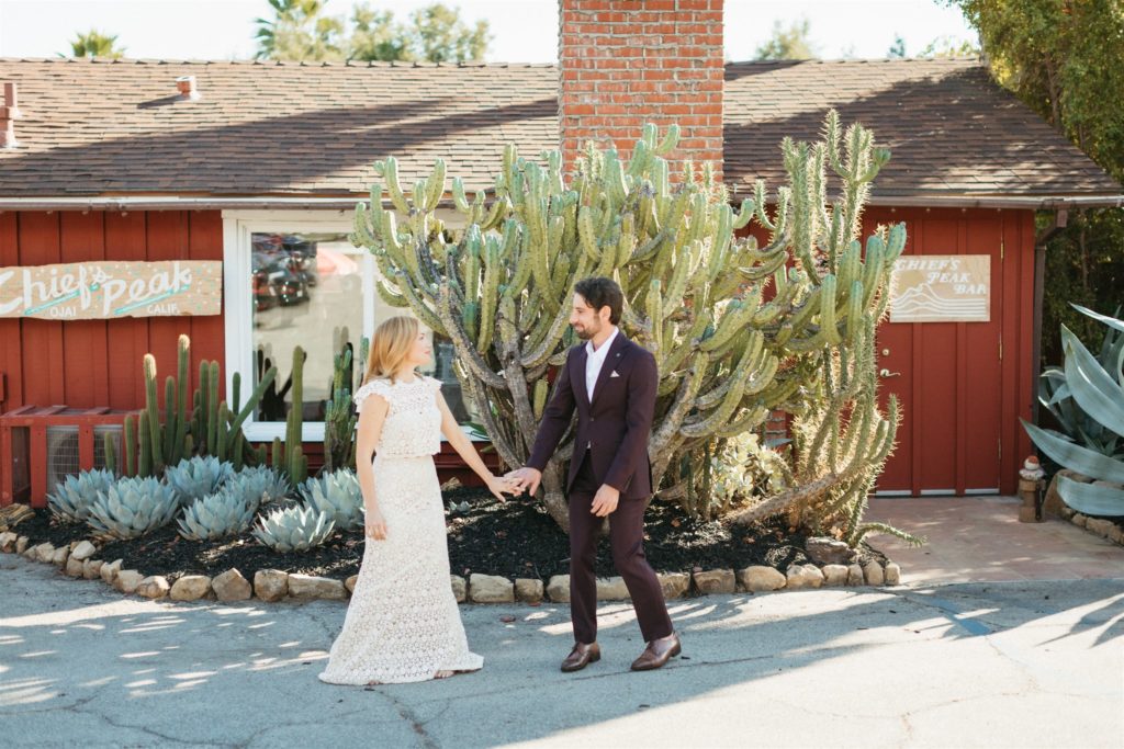 bride in two piece wedding dress and daisy in her hair does first look in front of cactus with groom in maroon suit with no tie