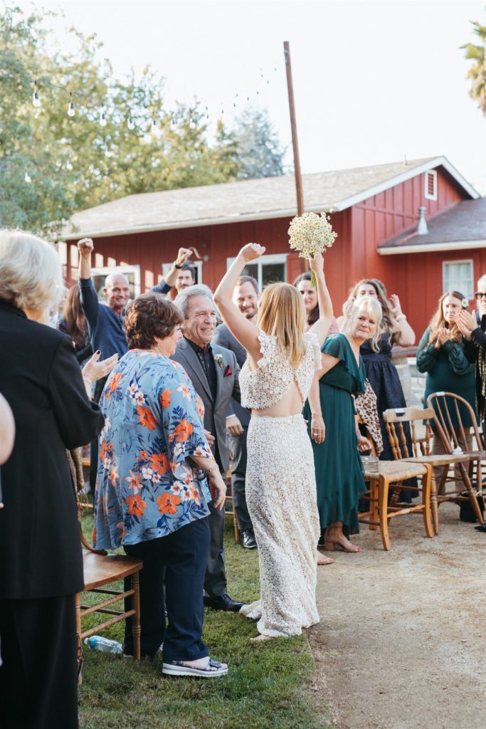 bride turns to guests with hands up before walking up altar during wedding