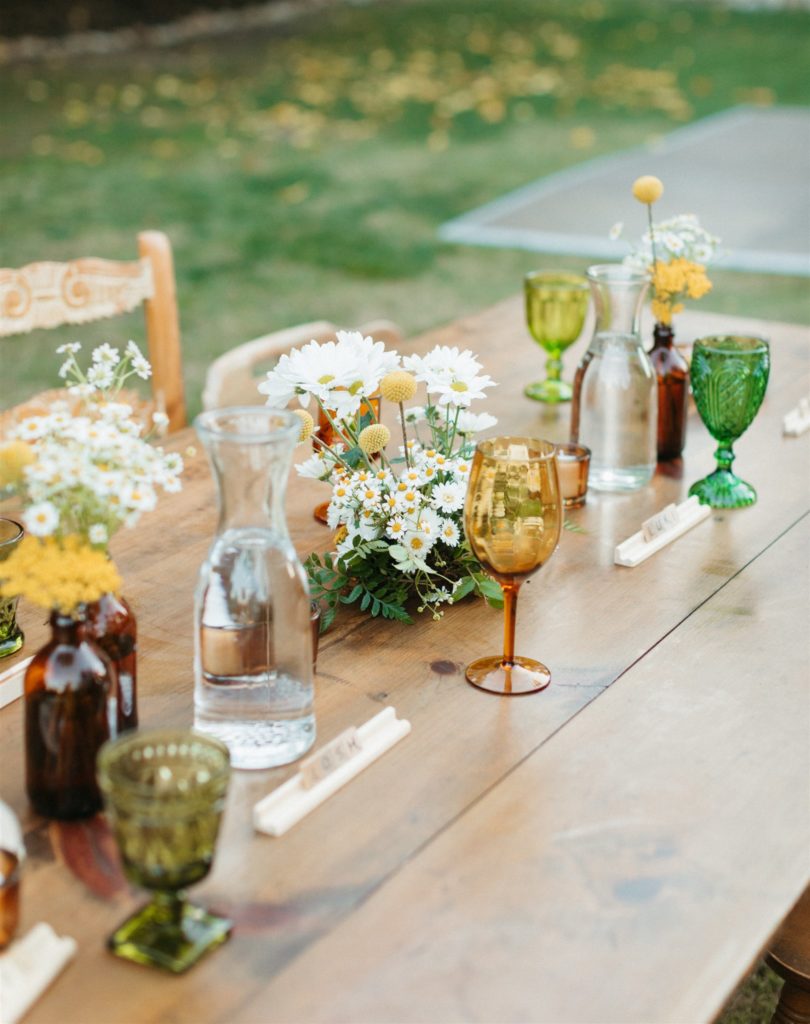 retro inspired wedding reception at Ojai Rancho Inn with wooden farm tables, mix matched wooden chairs and amber, green and yellow glassware with daisy centerpieces