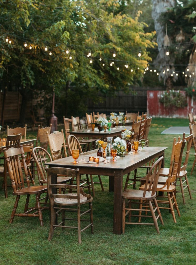 retro inspired wedding reception at Ojai Rancho Inn with wooden farm tables, mix matched wooden chairs and amber, green and yellow glassware with daisy centerpieces