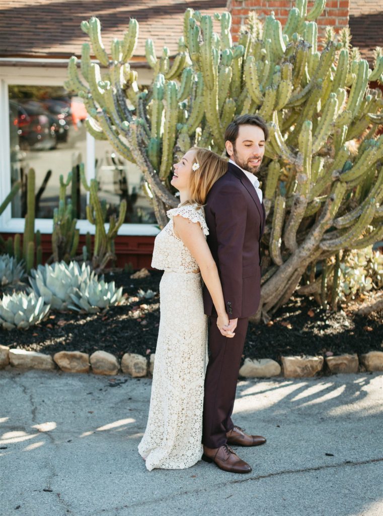 bride in two piece wedding dress and daisy in her hair does first look in front of cactus with groom in maroon suit with no tie