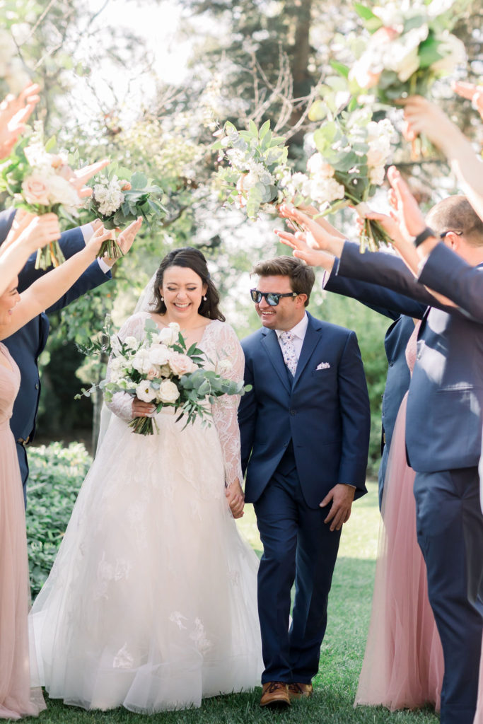 bride in long sleeve lace wedding dress with groom in blue suit taking wedding party photos at Maravilla Gardens