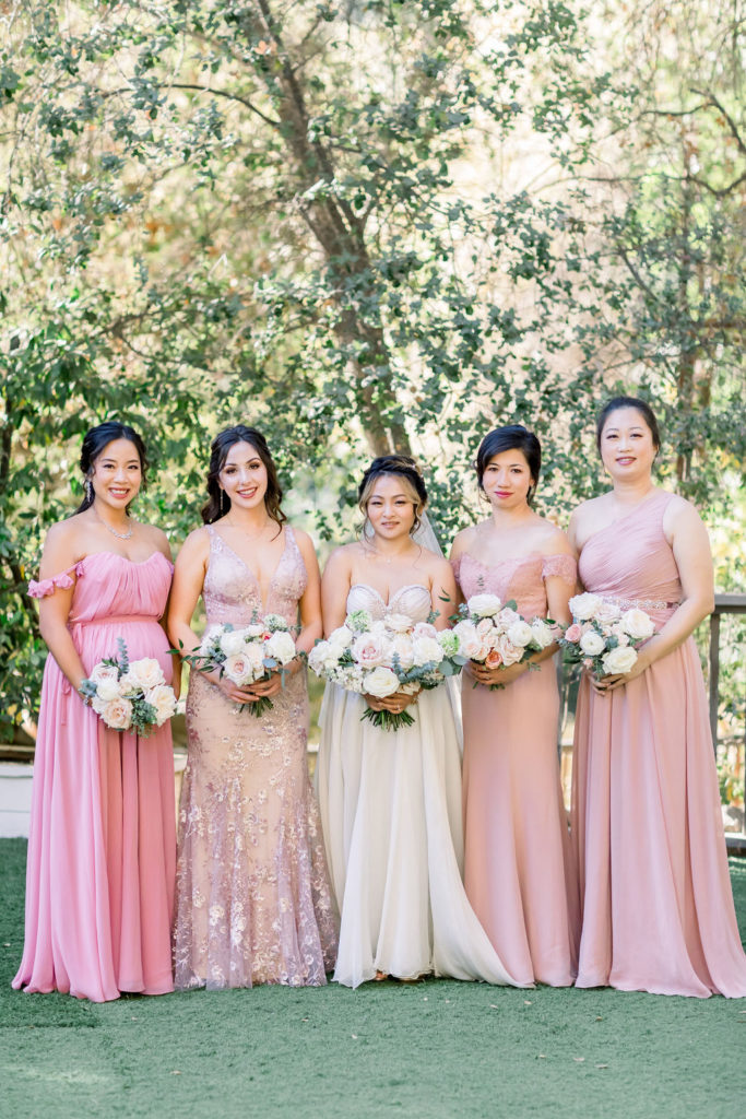 bride in beaded strapless wedding dress stands with her bridesmaids in mix matched pink dresses