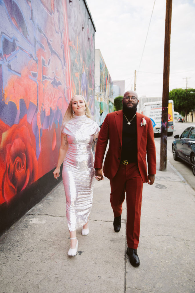 bride in silver dress with groom in red suit walk around DTLA