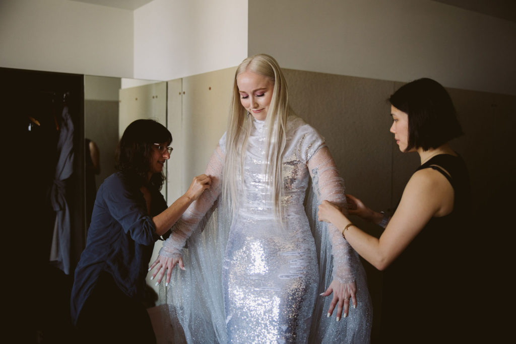 bride in silver wedding dress gets help from friends putting on silver sleeves