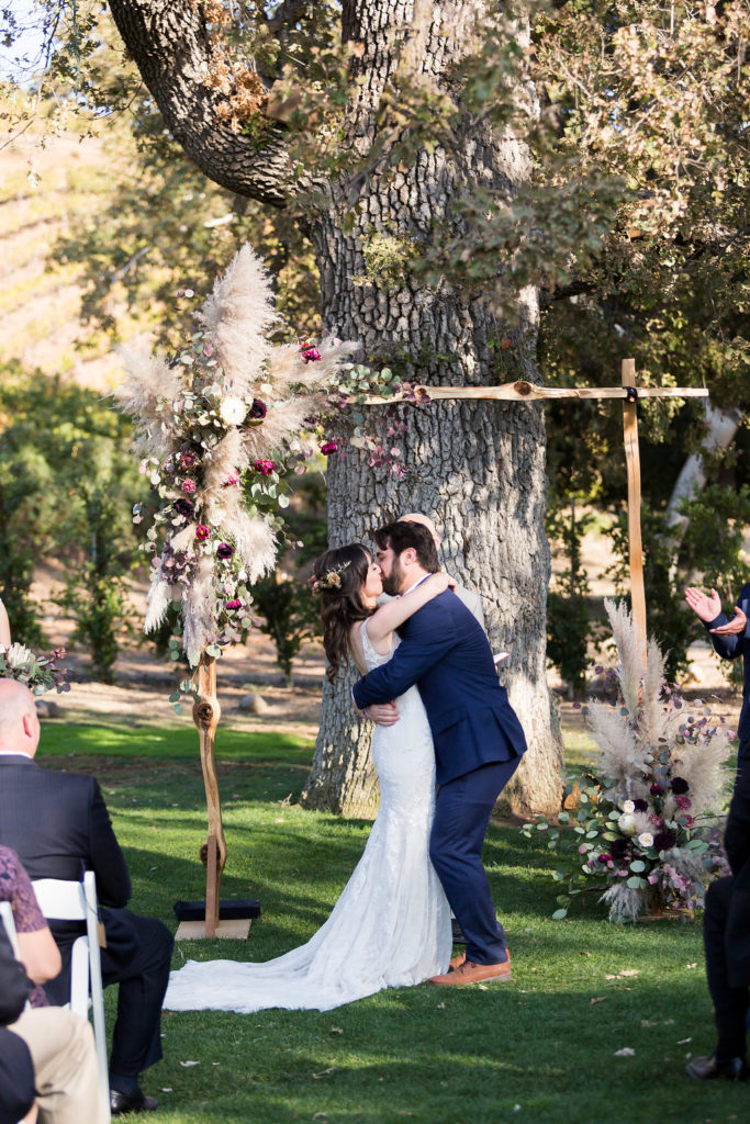 Wedding ceremony and first kiss at Triunfo Creek Vineyards with wooden arch