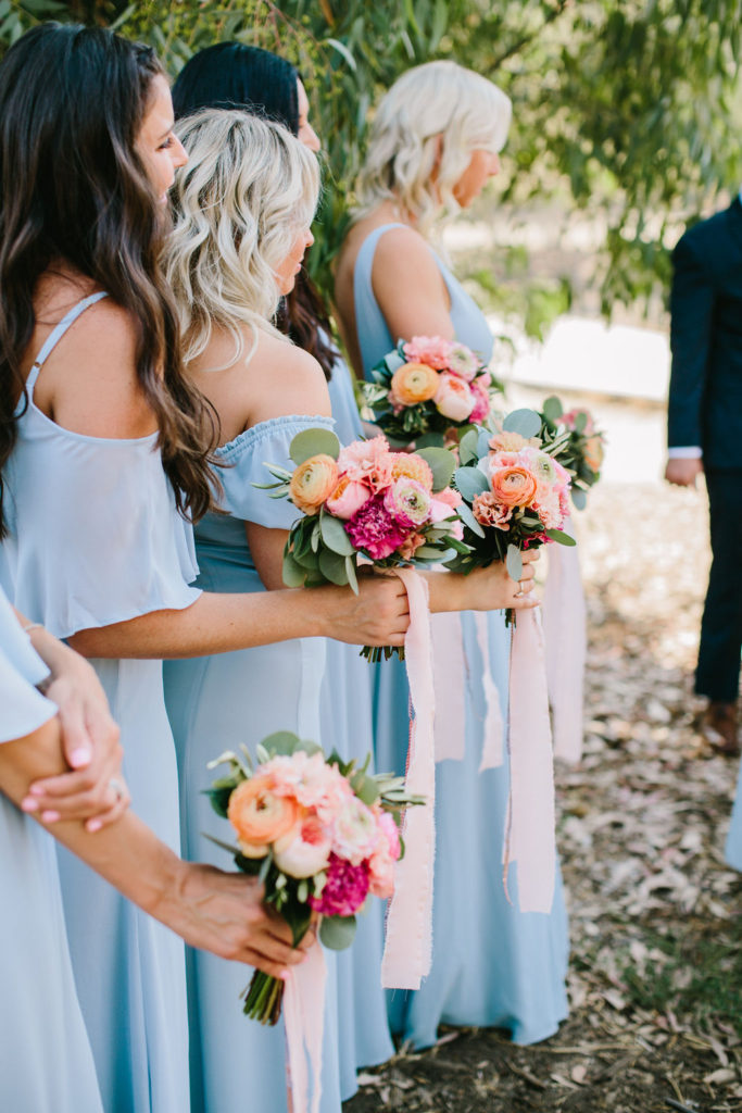 bridesmaids with blue dresses and bright pink and orange floral bouquets at wedding ceremony at Triunfo Creek Vineyards