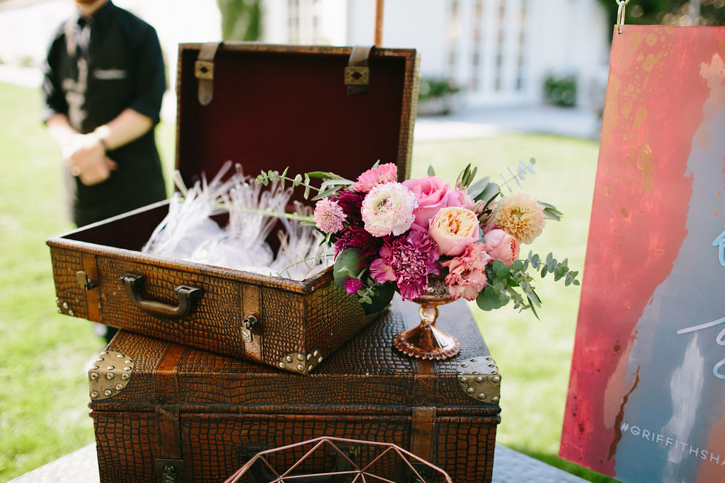 Wedding welcome table centerpiece with bright pink floral arrangement and vintage suitcase