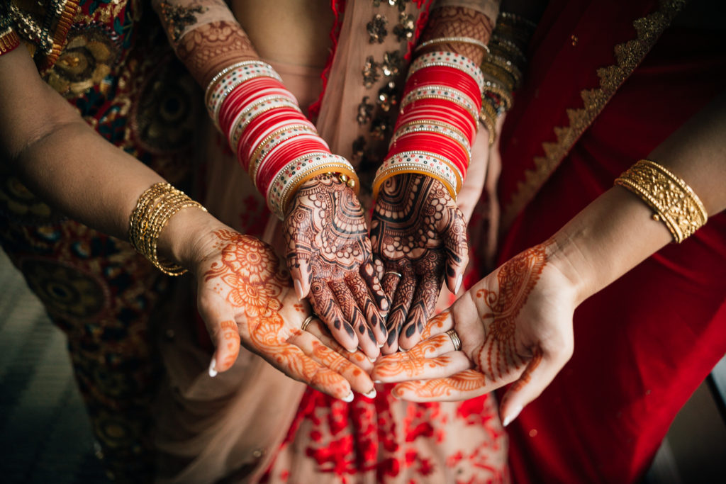 Stunning Indian Wedding in San Pedro, bride in gold and red wedding sari getting ready with henna tattoos and bracelets