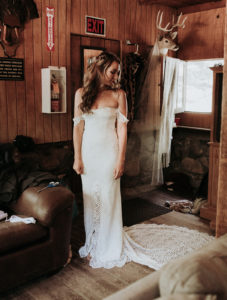 Summer camp themed wedding in Big Bear at Camp Wasegan, bride getting ready wearing a lace off the shoulder open back wedding dress