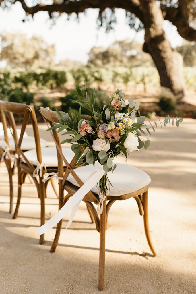 cross back ceremony chair with large floral arrangement tied to the side