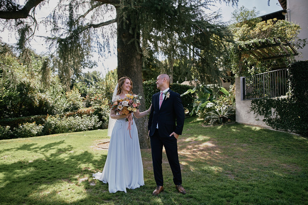 bride in vneck lace bodice wedding dress and groom in navy blue suit with pink tie have their first look at the historic Altadena Country Club