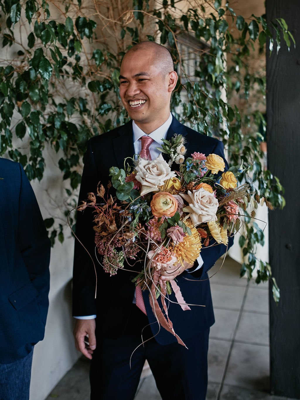 groom in navy suit holds brides wildflower bouquet