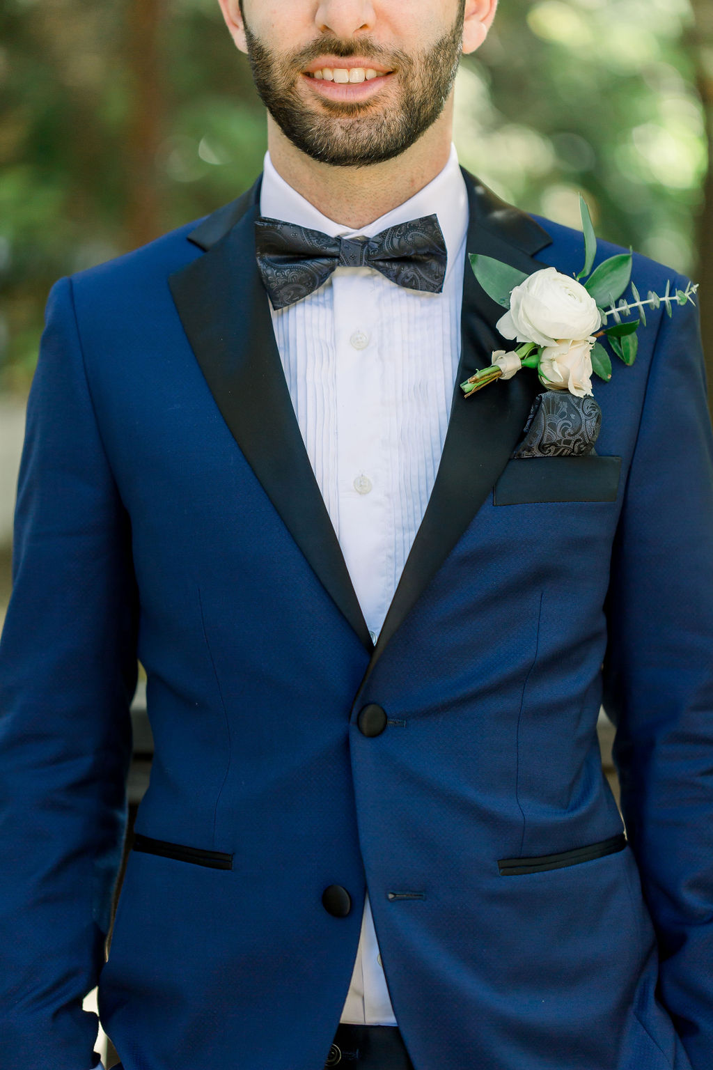 groom with paisley detail bowtie and blue tuxedo and white floral boutonniere 
