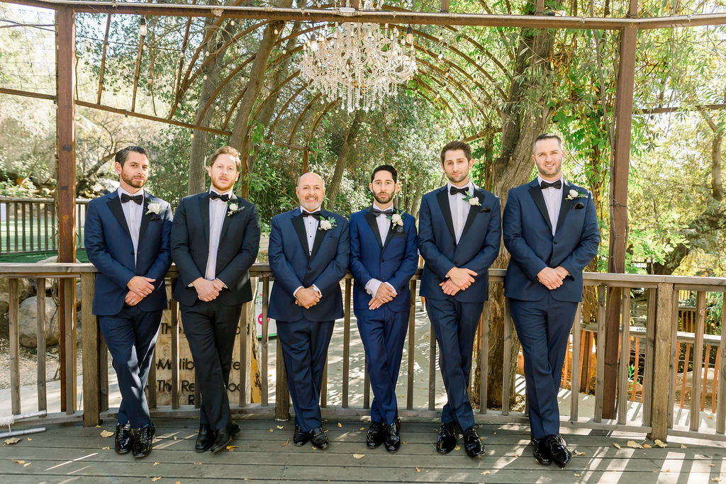 groom with paisley detail bowtie and blue tuxedo stands with groomsmen in navy suits 