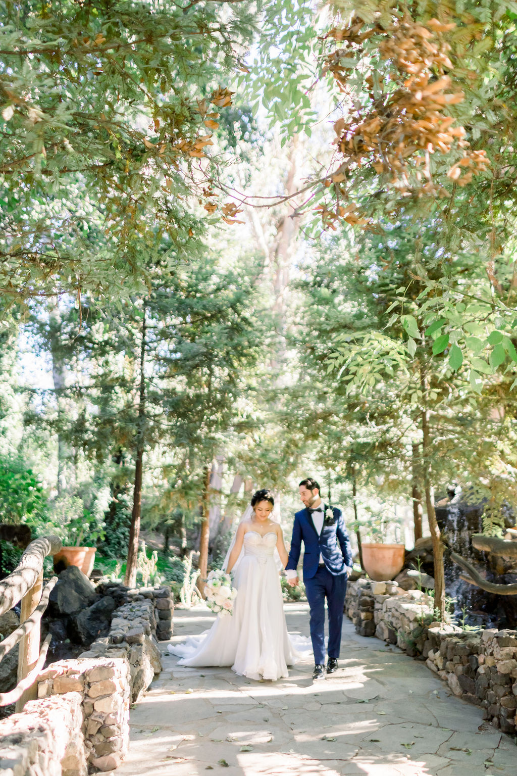 groom with paisley detail bowtie and blue tuxedo stands with bride in embellished chiffon strapless wedding dress at Calamigos Ranch