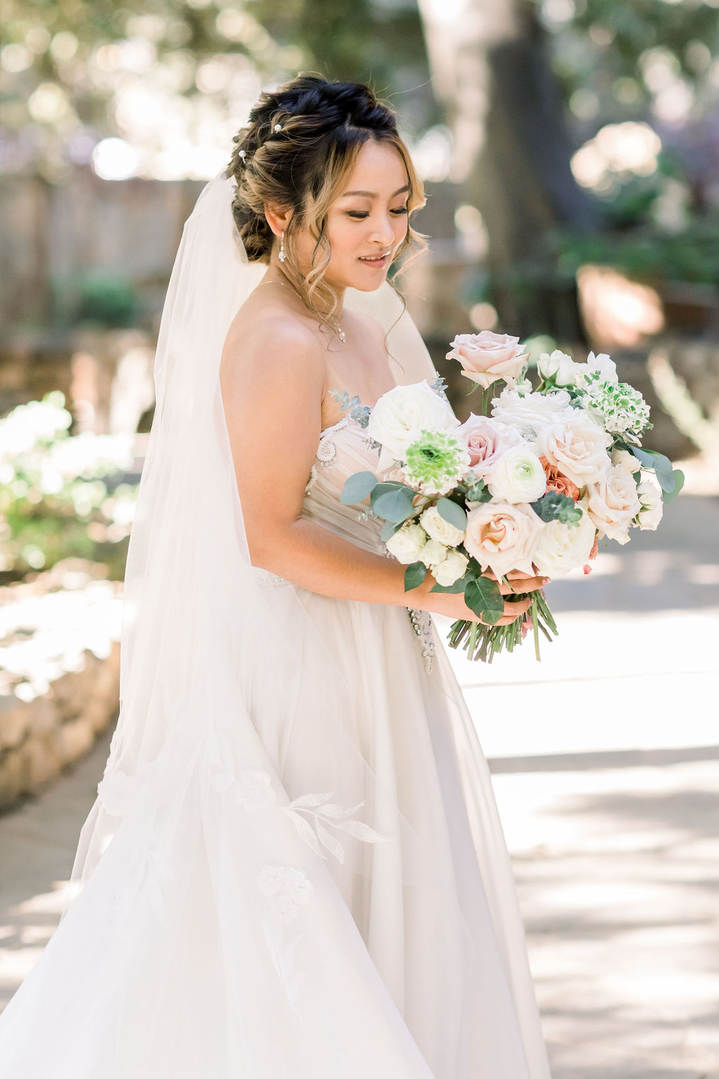 bride in embellished chiffon strapless wedding dress with long train and veil holding bouquet at Calamigos Ranch
