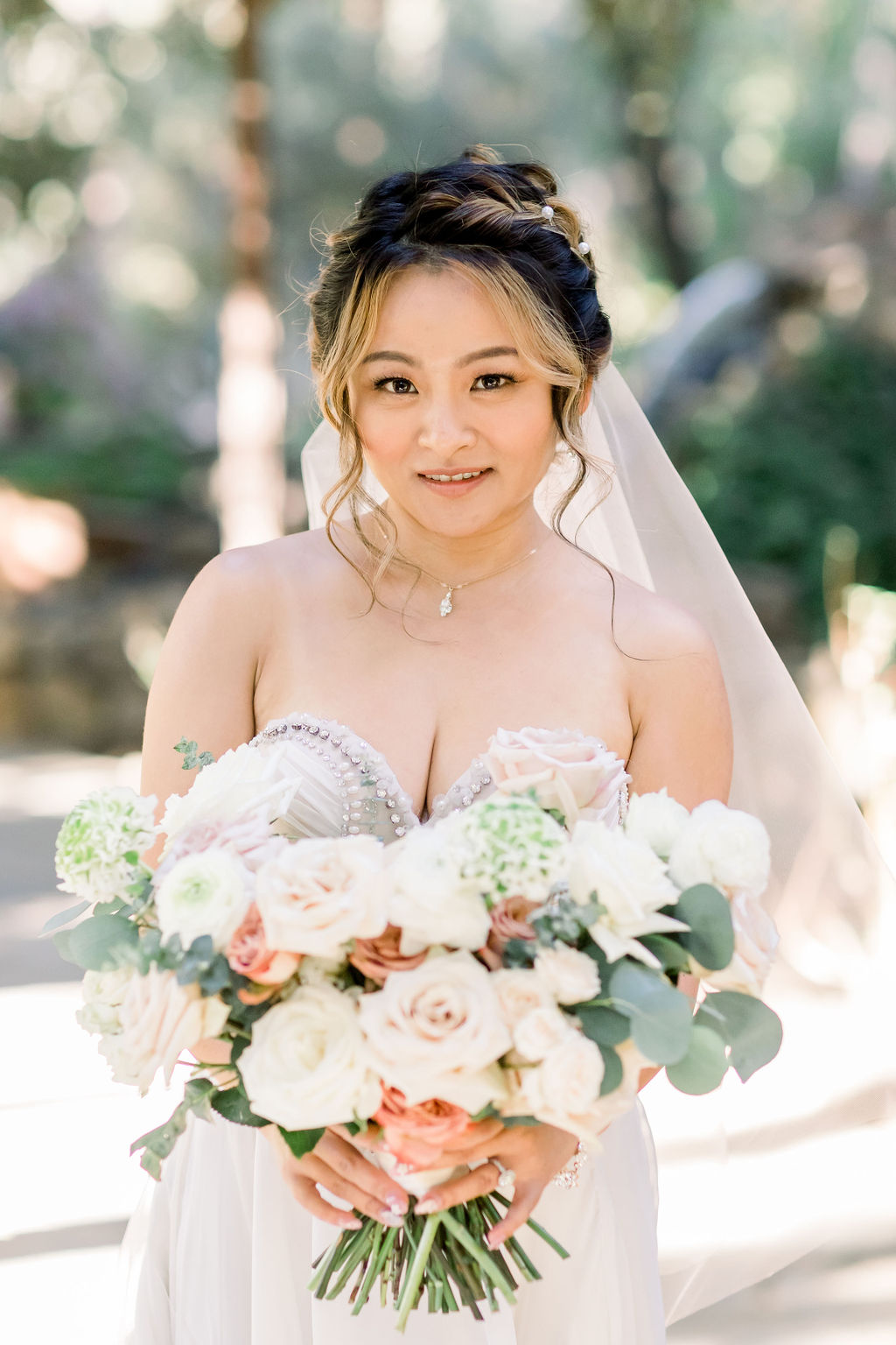 bride in embellished chiffon strapless wedding dress with long train and veil holding bouquet at Calamigos Ranch