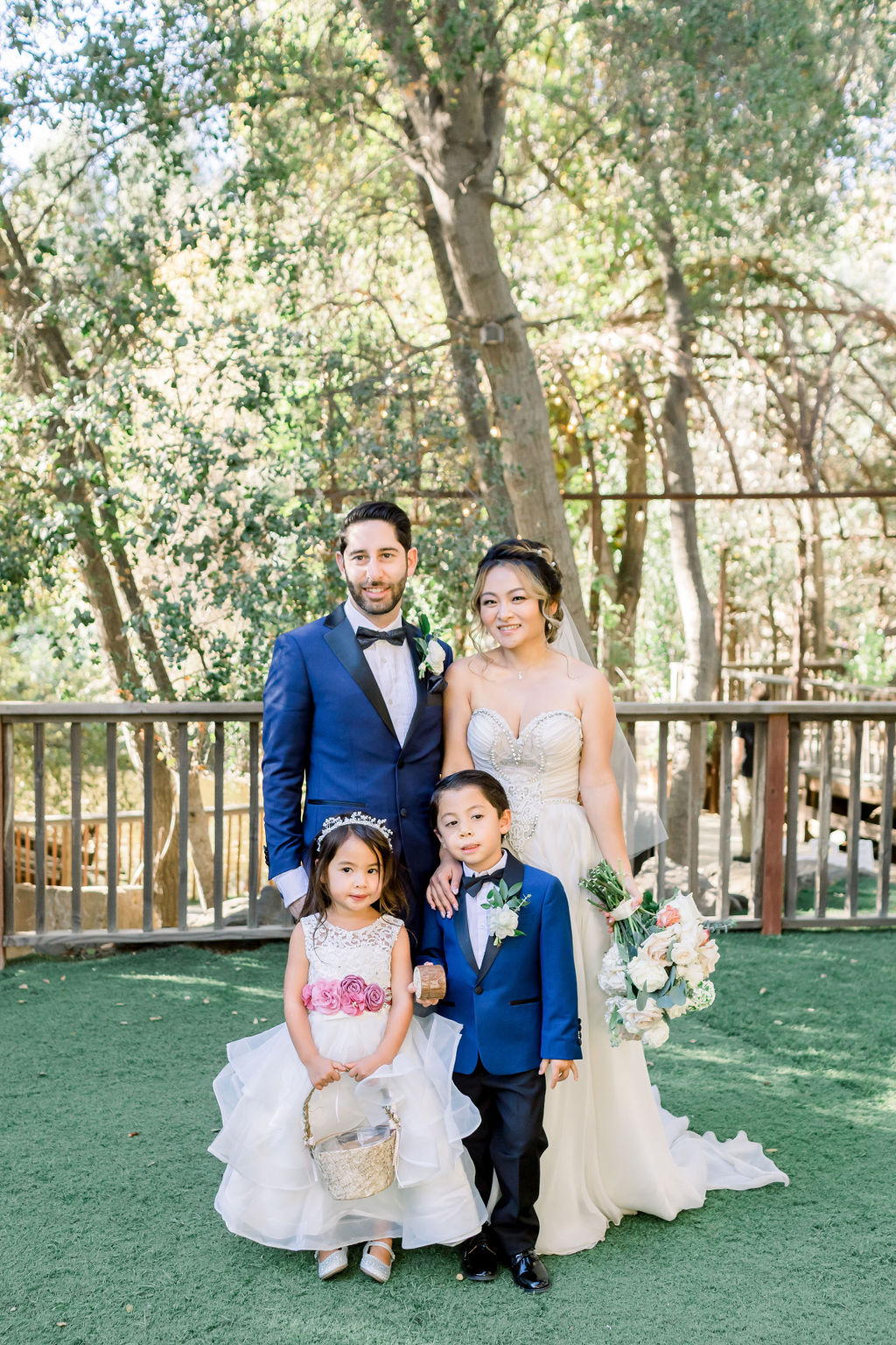 bride and groom stand with flower girl in white dress and ring bearer in blue suit
