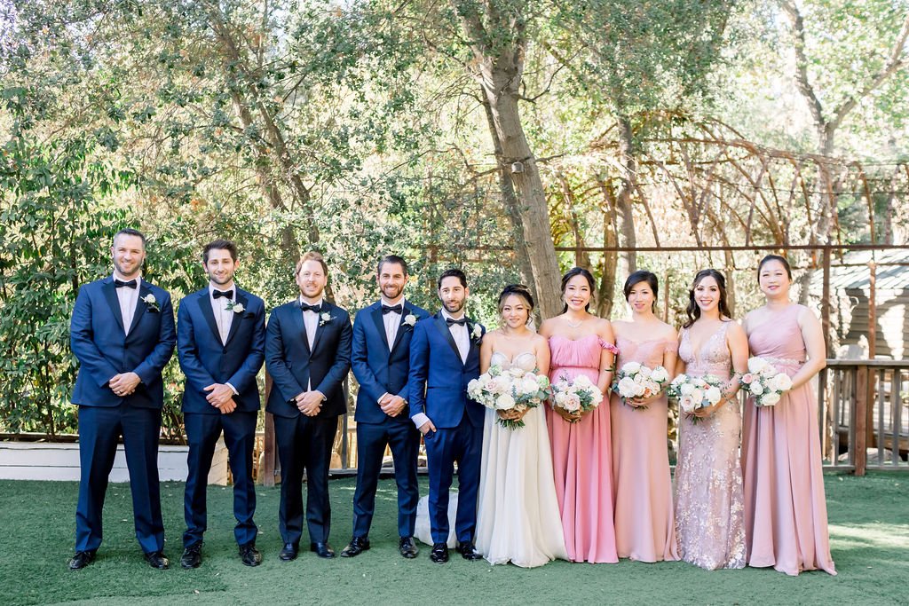bride and groom stand with wedding party in blue tuxedo suits and mix matched blush pink dresses