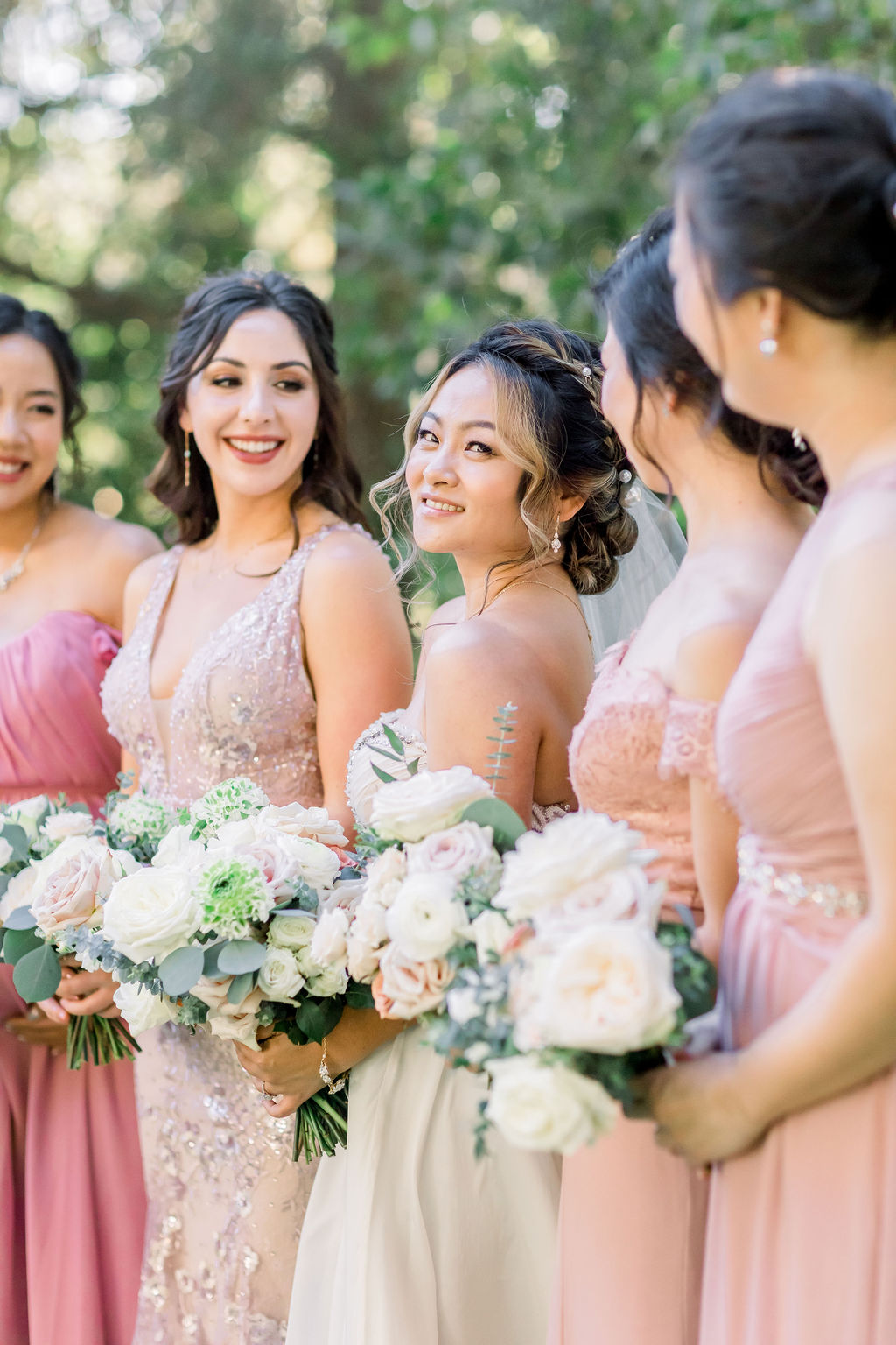 bride stands with bridesmaids in mix matched pink dresses