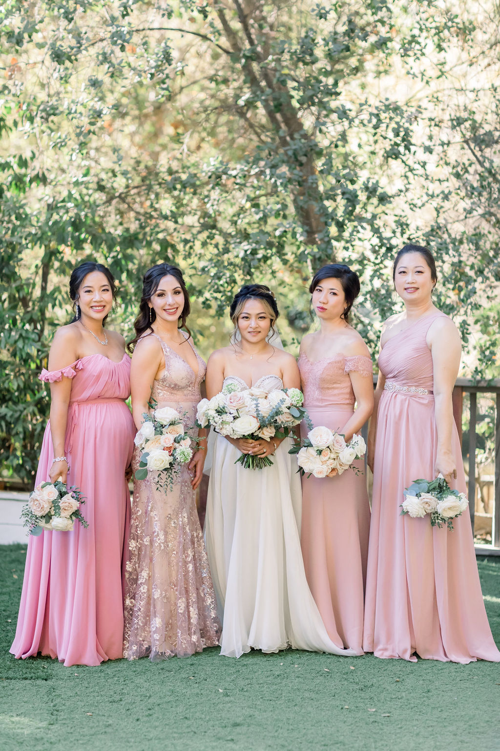 bride stands with bridesmaids in mix matched pink dresses