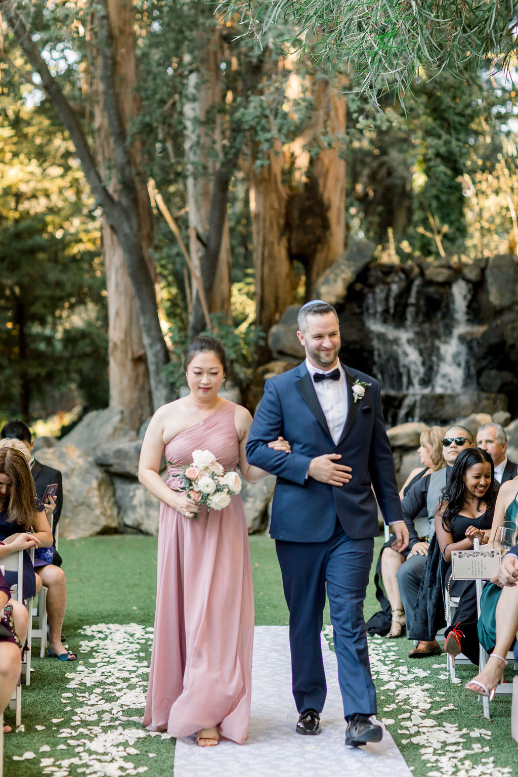 groomsman in blue suit walks with bridesmaid in blush pink dress