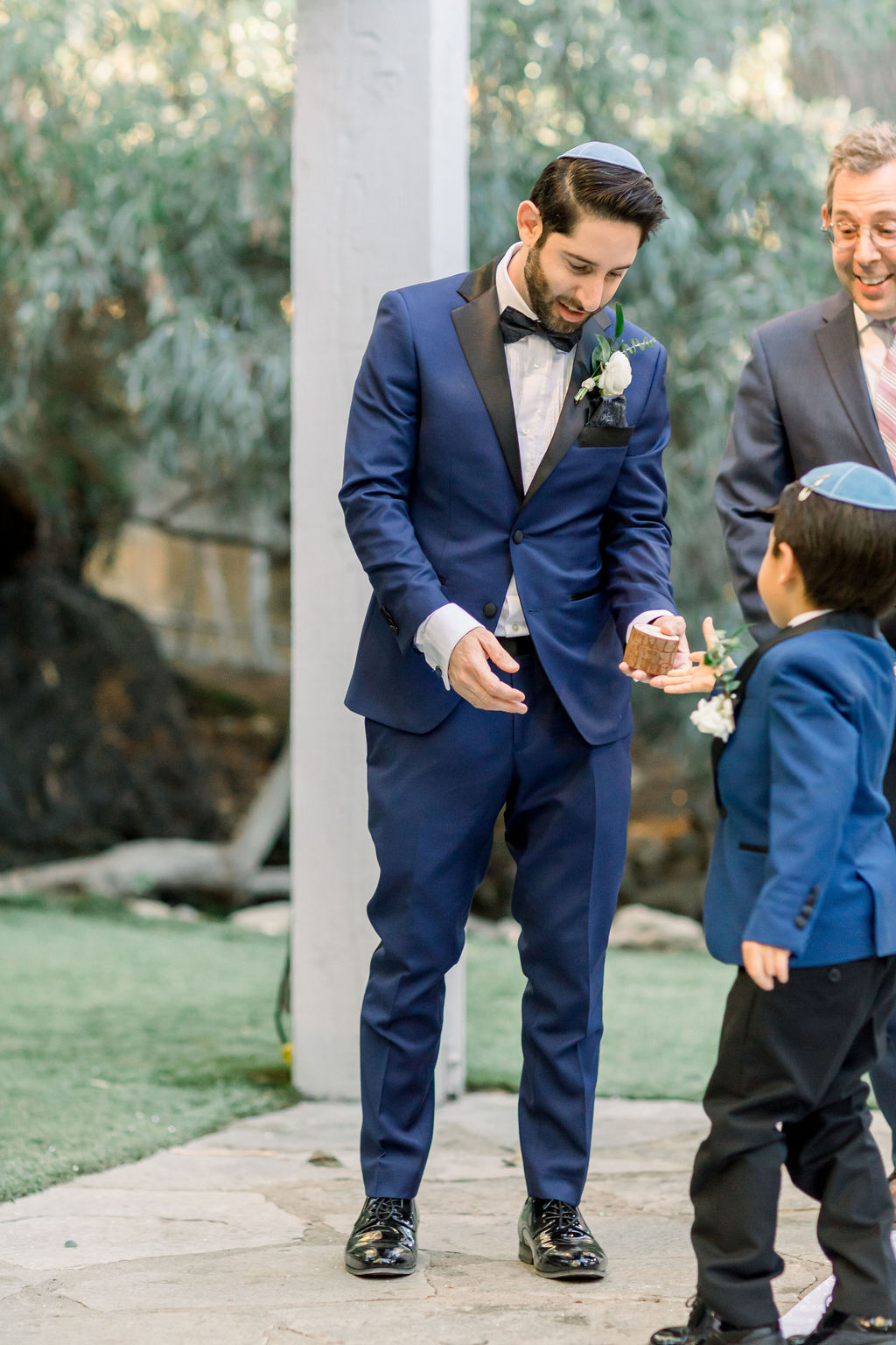ring bearer in blue suit hands groom wooden ring box during wedding ceremony