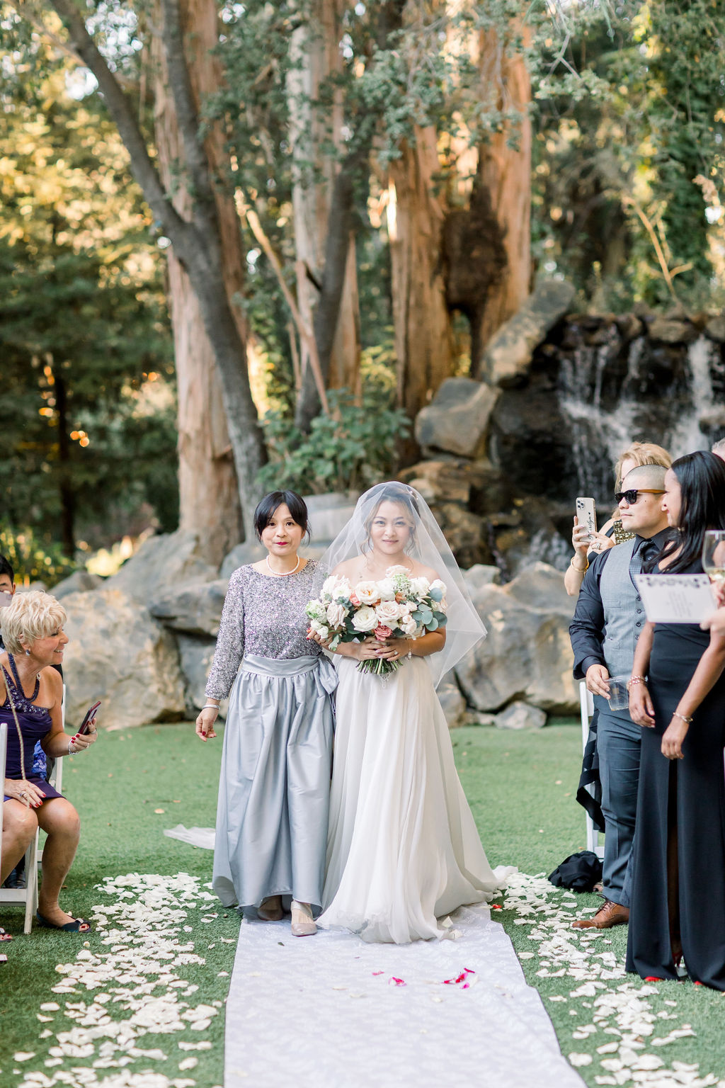 bride walks with mother in silver dress down aisle