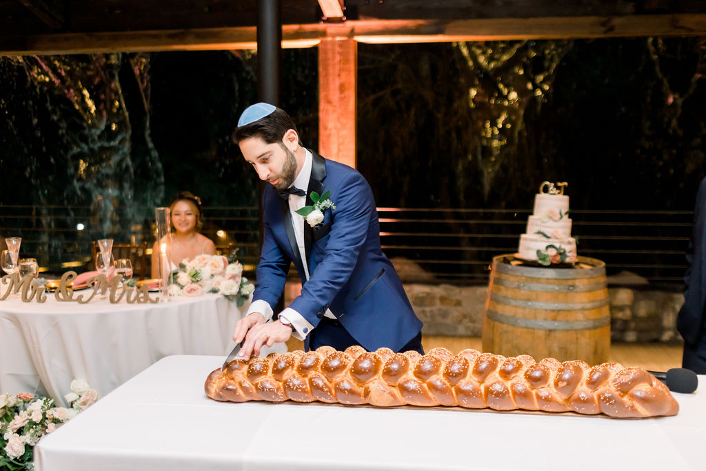 groom cuts into challah bread during wedding reception