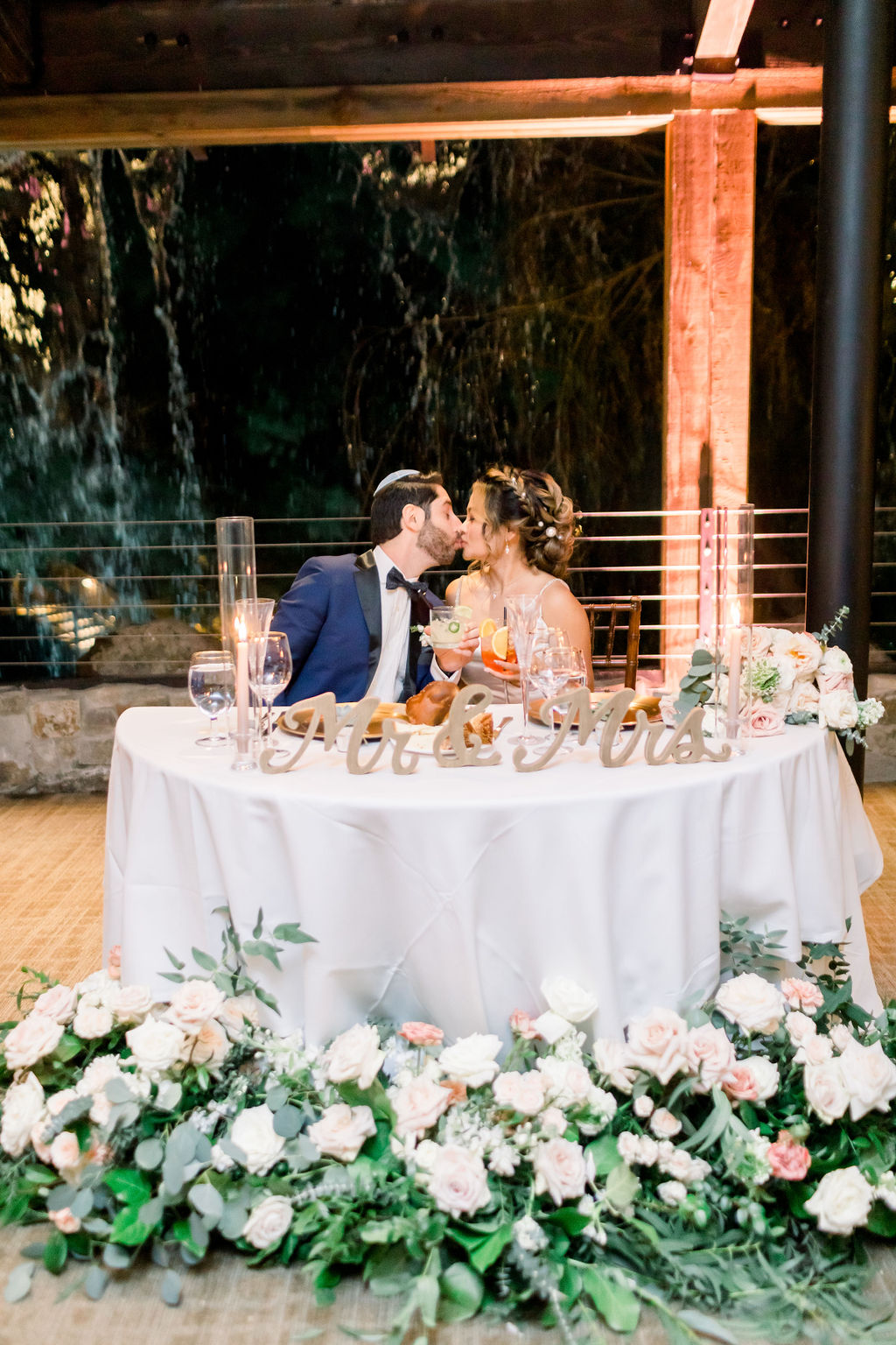 bride and groom kiss at sweetheart table during wedding reception