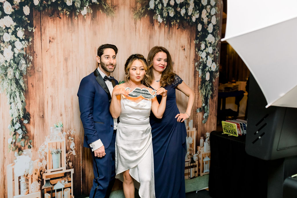 bride in silk reception dress takes photo in Photo Booth with groom in blue suit