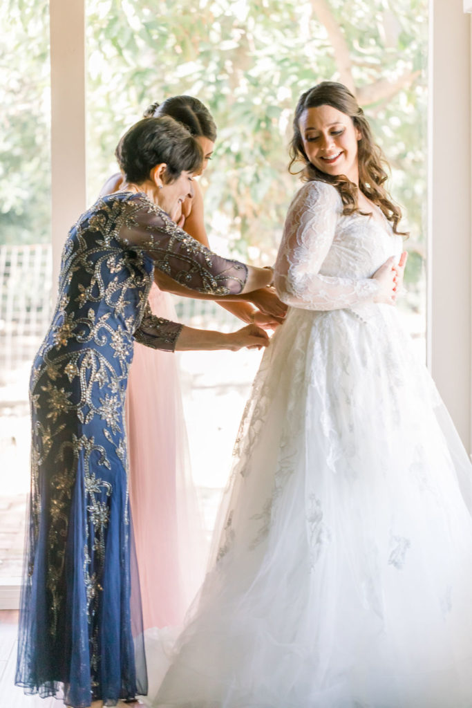 bride getting into long sleeve lace wedding dress with sweetheart neckline and floral appliqué 