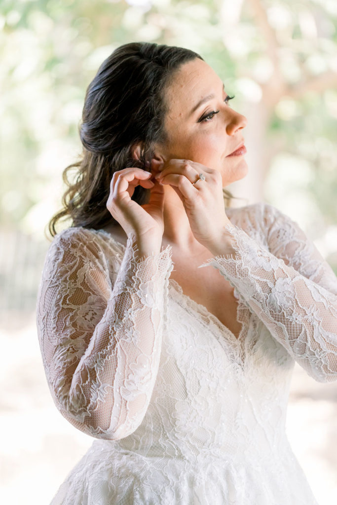 bride putting on jewelry wearing long sleeve lace wedding dress with sweetheart neckline and floral appliqué 