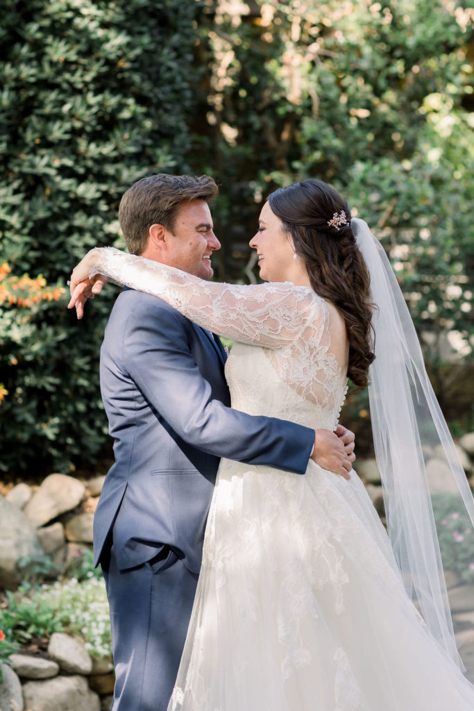 bride in long sleeve lace wedding dress with groom in blue suit and floral tie take wedding portrait shots at Maravilla Gardens