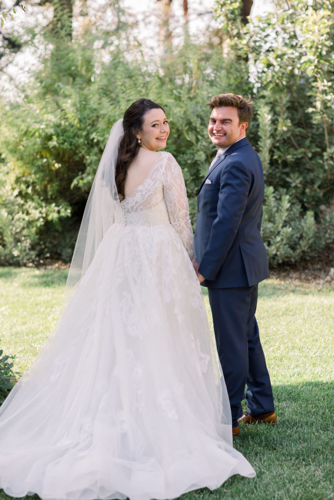 bride in long sleeve lace wedding dress with groom in blue suit and floral tie take wedding portrait shots at Maravilla Gardens