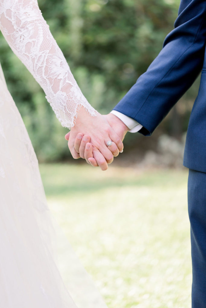 up close photo of bride in long sleeve wedding dress holding hands with groom in blue suit