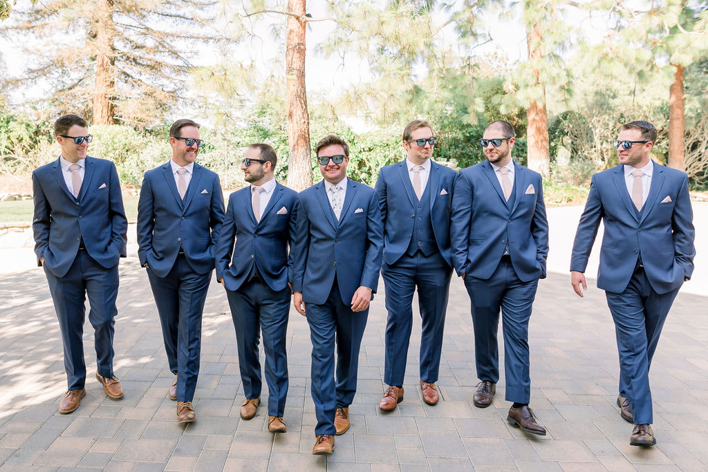 groom and groomsmen in glasses and blue suits with floral and pink ties