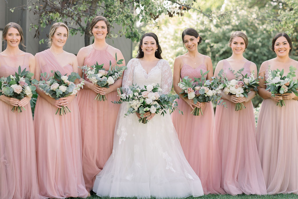 bride in long sleeve wedding dress with bridesmaids in pink dresses holding romantic bouquets