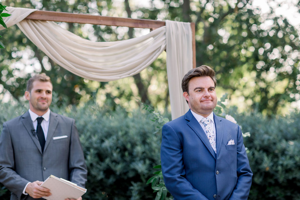 groom in blue suit and floral tie waits at the aisle