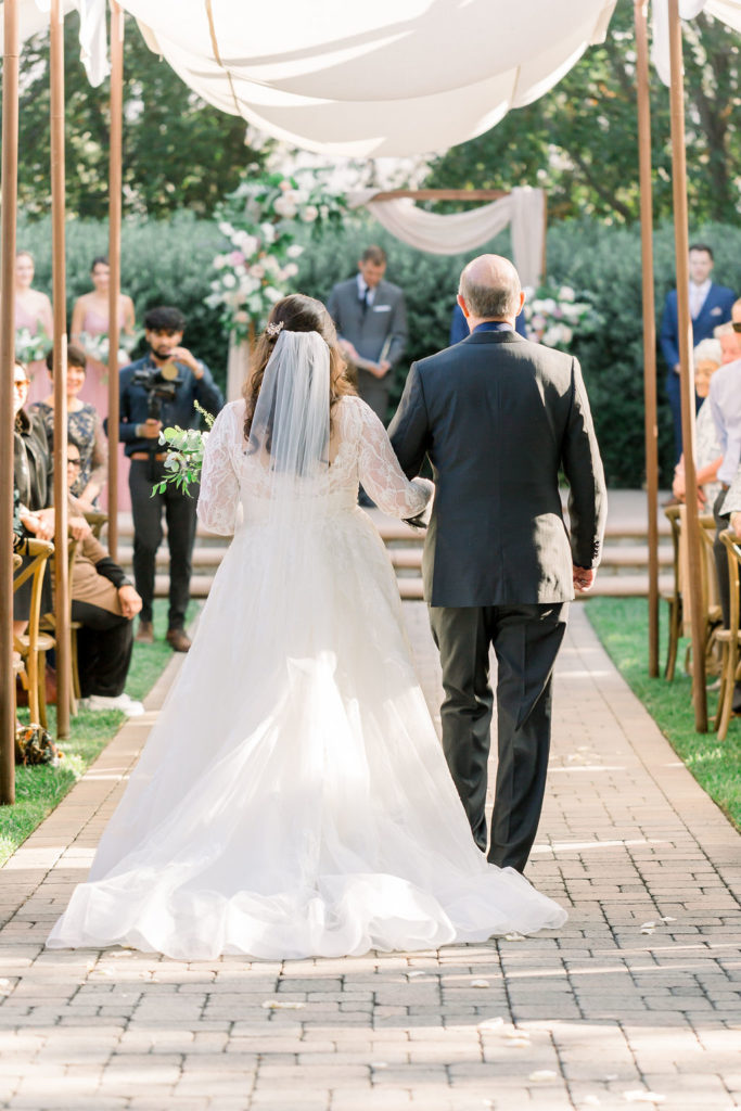 bride with long veil in hair walks down the aisle with father