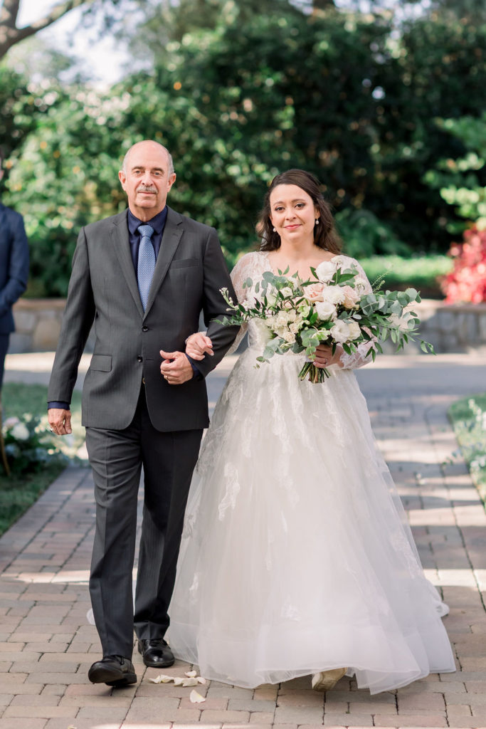 bride in long sleeve wedding dress walks down the aisle with father 